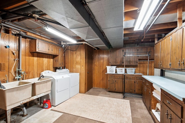 laundry room with washer and clothes dryer, a sink, cabinet space, wood walls, and light floors