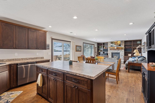 kitchen with a kitchen island, dark brown cabinetry, a stone fireplace, light wood-style floors, and stainless steel dishwasher