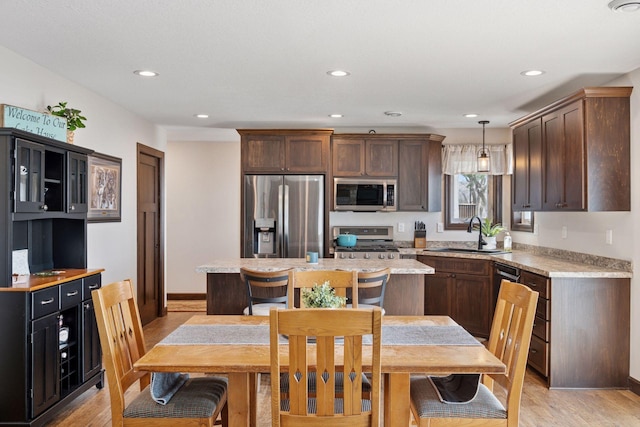 kitchen with pendant lighting, light wood-type flooring, light countertops, stainless steel appliances, and a sink