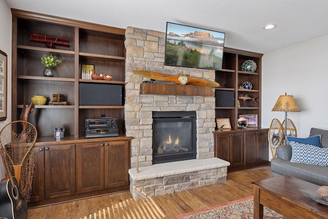 living room featuring a stone fireplace, recessed lighting, and wood finished floors