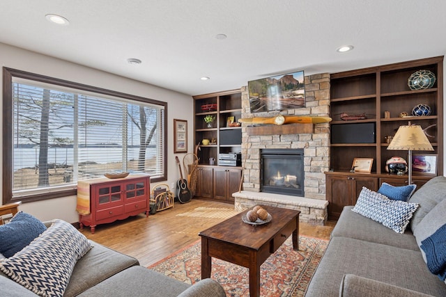 living room with recessed lighting, light wood-style flooring, a fireplace, and built in features