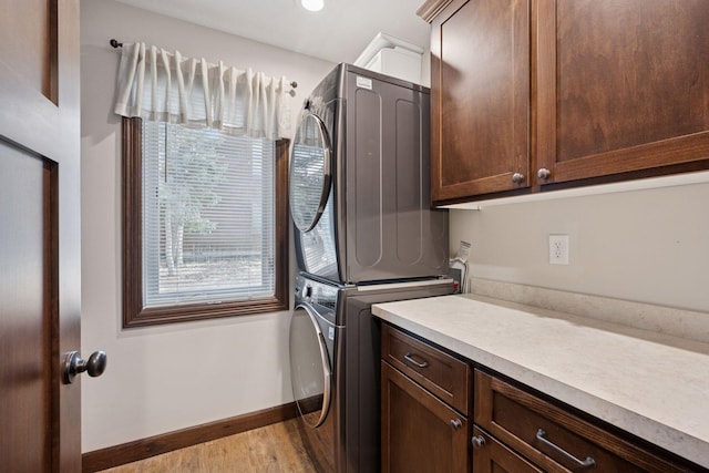 washroom featuring baseboards, cabinet space, stacked washing maching and dryer, and light wood-style floors