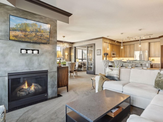 living area featuring light carpet, ornamental molding, track lighting, an inviting chandelier, and a fireplace