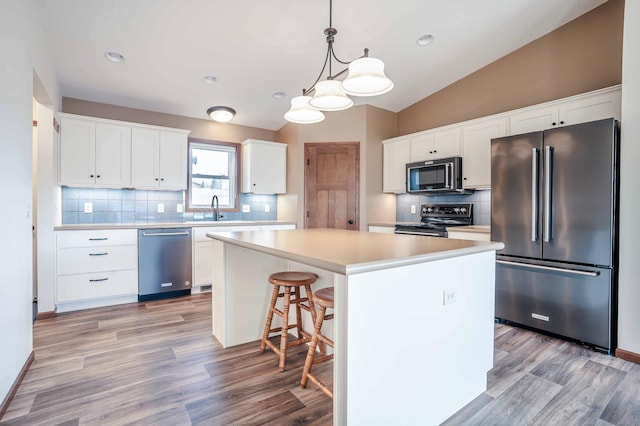 kitchen featuring a sink, a center island, stainless steel appliances, white cabinets, and vaulted ceiling