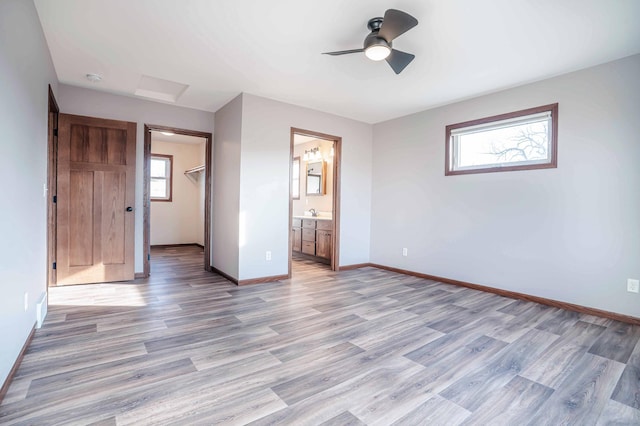 unfurnished bedroom with a spacious closet, connected bathroom, baseboards, ceiling fan, and light wood-style floors