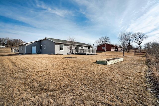 rear view of house with a yard, a wooden deck, and fence