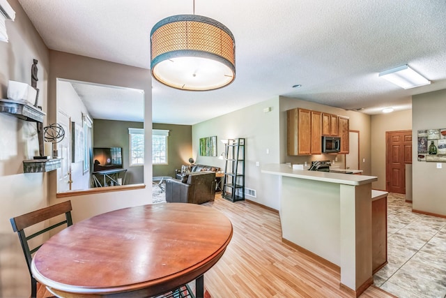 dining space with visible vents, light wood-style floors, baseboards, and a textured ceiling