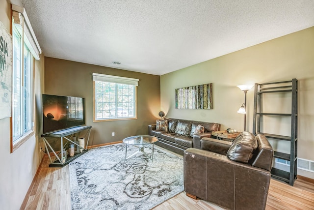 living room with baseboards, a textured ceiling, and light wood finished floors