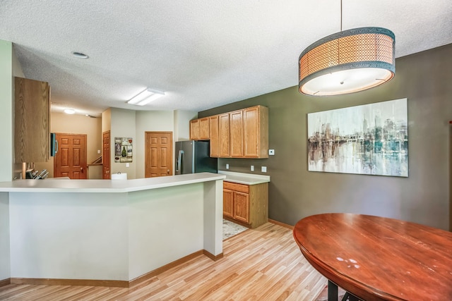 kitchen featuring a peninsula, light countertops, light wood-style floors, stainless steel refrigerator with ice dispenser, and a textured ceiling