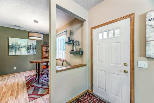 foyer entrance featuring baseboards, a textured ceiling, and wood finished floors