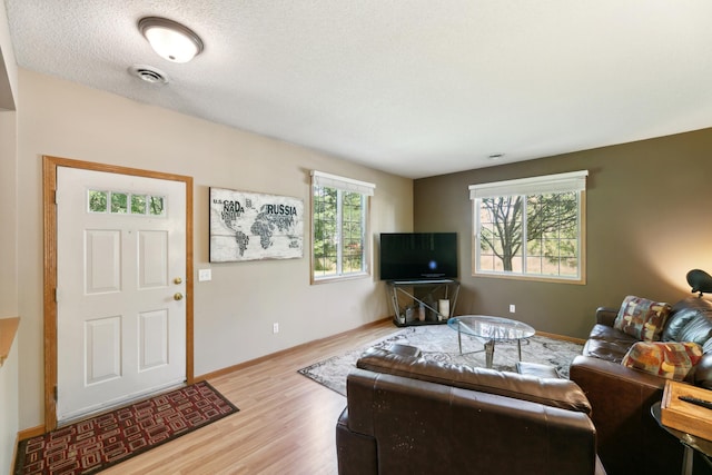 living room with plenty of natural light, light wood-style flooring, visible vents, and baseboards