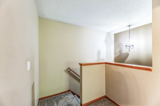 stairs featuring a notable chandelier, baseboards, carpet, and a textured ceiling