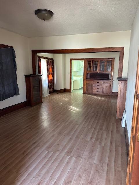 unfurnished living room featuring a textured ceiling, baseboards, and wood finished floors