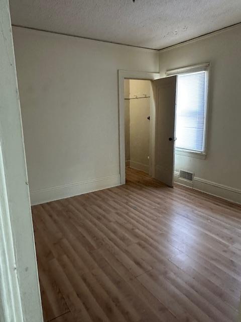 unfurnished bedroom featuring visible vents, a textured ceiling, baseboards, and wood finished floors