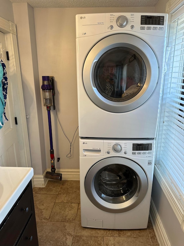 laundry area with light tile patterned floors, a textured ceiling, baseboards, and stacked washer and dryer