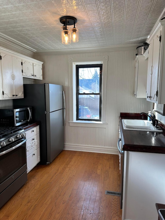 kitchen with light wood-style flooring, ornamental molding, a sink, appliances with stainless steel finishes, and dark countertops