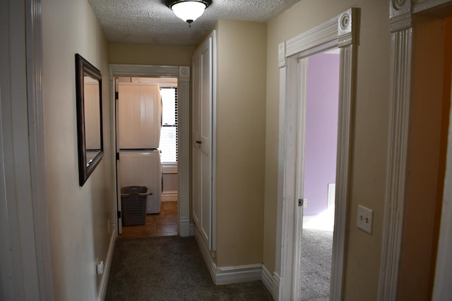 corridor with baseboards, dark colored carpet, and a textured ceiling