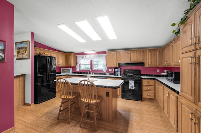 kitchen featuring a center island, under cabinet range hood, a breakfast bar area, vaulted ceiling, and black appliances