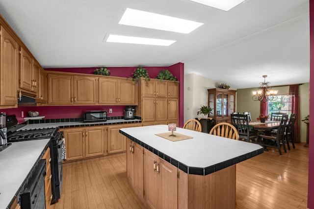 kitchen featuring light wood finished floors, a kitchen island, black appliances, and vaulted ceiling