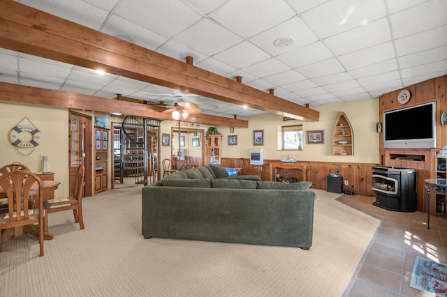 living area with a wainscoted wall, a wood stove, stairs, a paneled ceiling, and wood walls