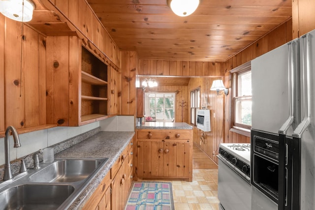 kitchen featuring a peninsula, a sink, white gas range oven, wood walls, and black fridge