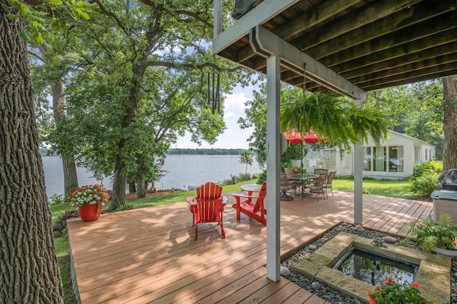 wooden terrace featuring a lawn, outdoor dining area, and a water view