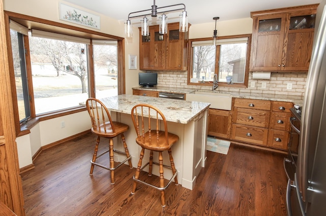 kitchen featuring brown cabinetry, a kitchen island, dark wood finished floors, a sink, and decorative backsplash