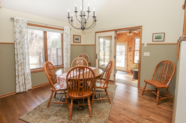 dining space with vaulted ceiling, ceiling fan with notable chandelier, baseboards, and wood finished floors