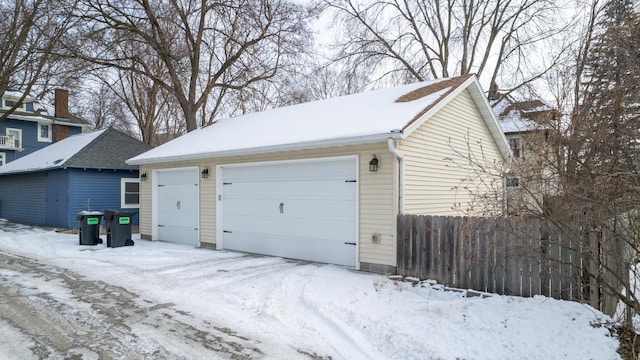 snow covered garage with a detached garage and fence