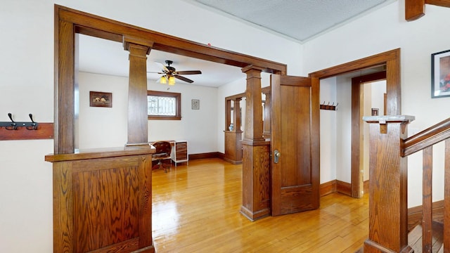 hallway featuring baseboards, light wood finished floors, and ornate columns