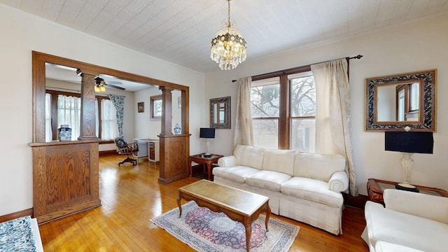 living area featuring light wood-type flooring, baseboards, ornamental molding, decorative columns, and ceiling fan with notable chandelier