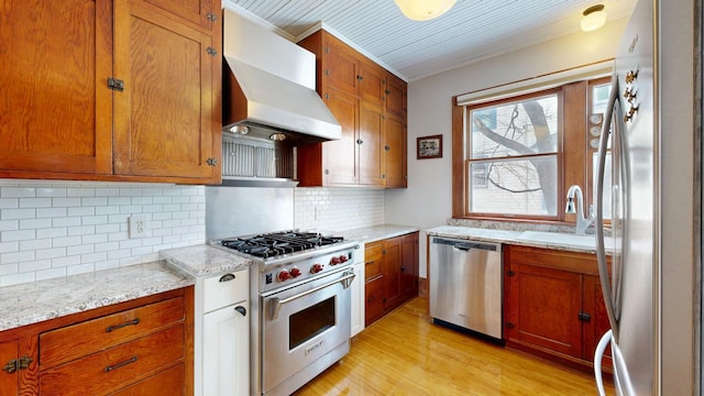 kitchen featuring light wood-type flooring, wall chimney range hood, ornamental molding, a sink, and stainless steel appliances