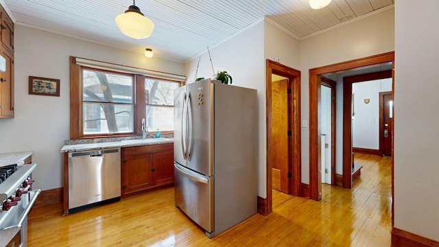 kitchen featuring light wood-style floors, ornamental molding, appliances with stainless steel finishes, a sink, and brown cabinets