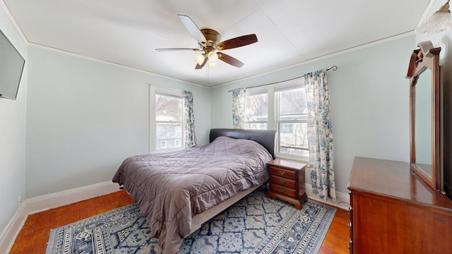 bedroom featuring wood finished floors, ornamental molding, baseboards, and a ceiling fan