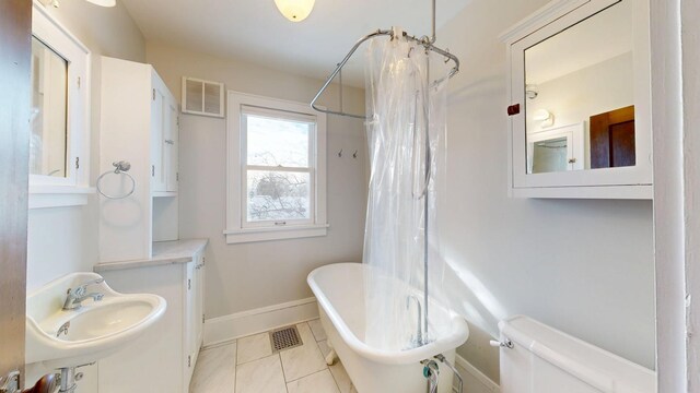 bathroom featuring baseboards, a soaking tub, a sink, and visible vents