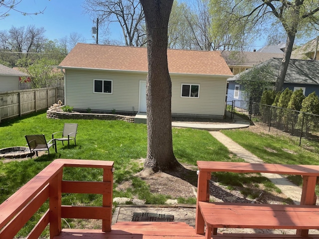 back of house with an outdoor fire pit, a yard, a shingled roof, and a fenced backyard