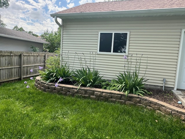 view of side of property with a shingled roof, fence, and a lawn