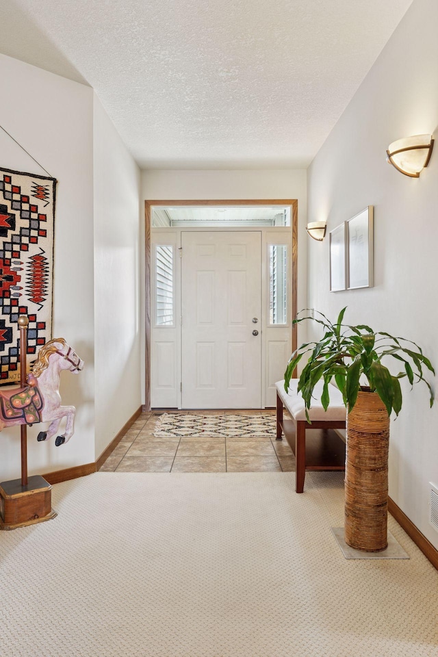 carpeted foyer entrance with visible vents, baseboards, and a textured ceiling