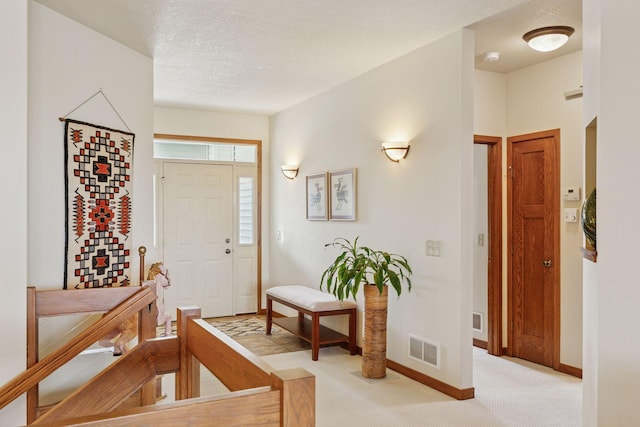 foyer entrance with a textured ceiling, baseboards, visible vents, and light carpet