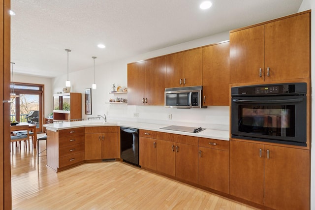 kitchen with light wood-type flooring, a peninsula, brown cabinetry, black appliances, and a sink