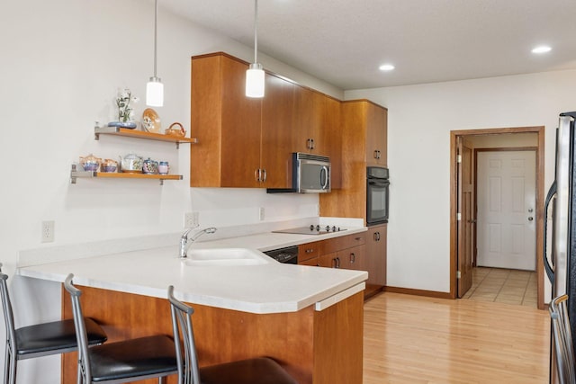 kitchen with a kitchen bar, a peninsula, brown cabinetry, black appliances, and a sink