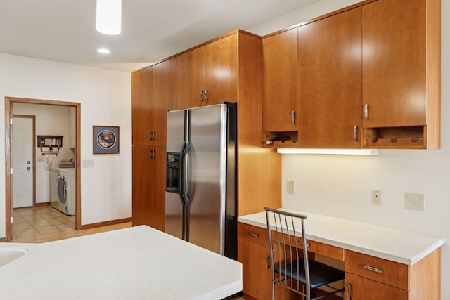 kitchen featuring brown cabinetry, stainless steel fridge with ice dispenser, light countertops, built in desk, and independent washer and dryer