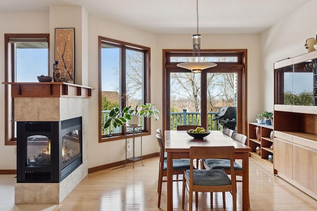 dining area with light wood-style flooring, baseboards, and a tile fireplace