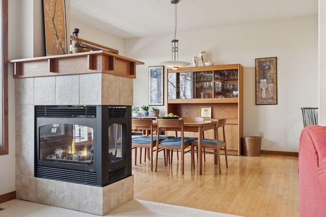 dining space featuring a multi sided fireplace, baseboards, and wood finished floors