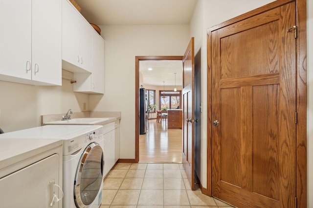 clothes washing area featuring washing machine and clothes dryer, baseboards, light tile patterned flooring, cabinet space, and a sink