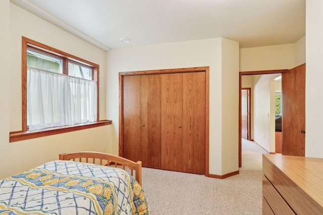 bedroom with a closet, light colored carpet, and baseboards