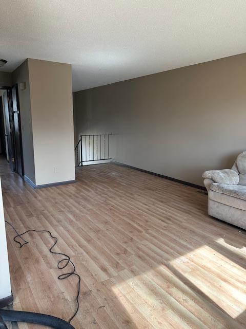 unfurnished living room featuring wood finished floors, baseboards, and a textured ceiling