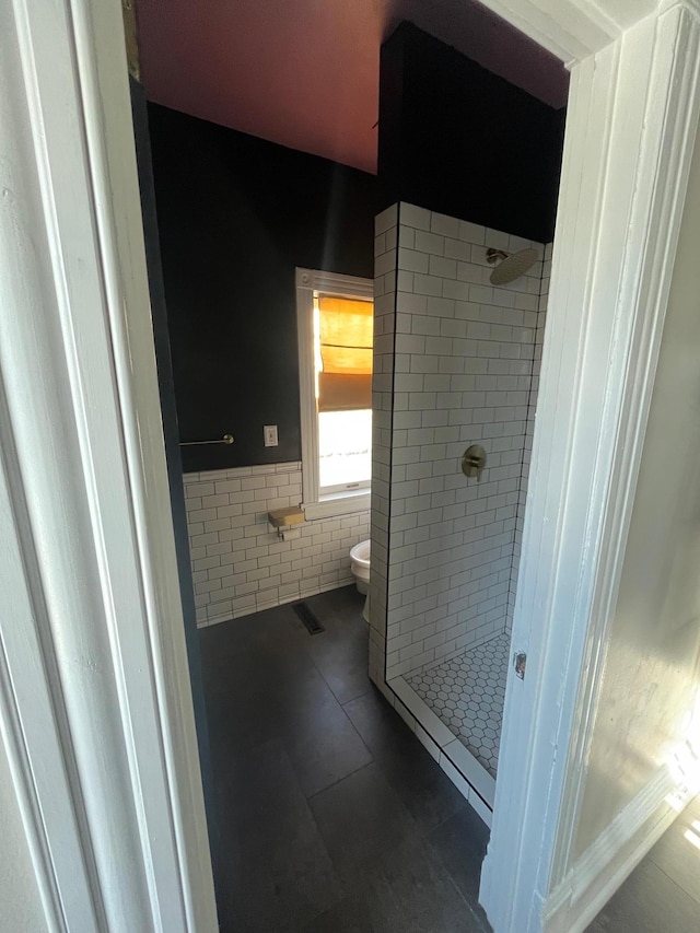 bathroom featuring a wainscoted wall, a stall shower, tile patterned flooring, tile walls, and toilet