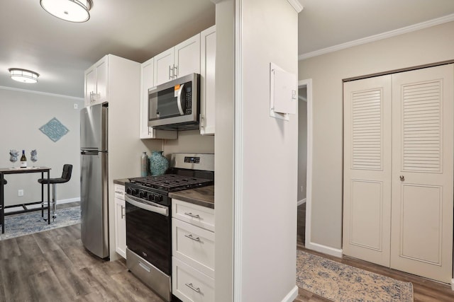 kitchen with dark countertops, ornamental molding, appliances with stainless steel finishes, dark wood-style floors, and white cabinets