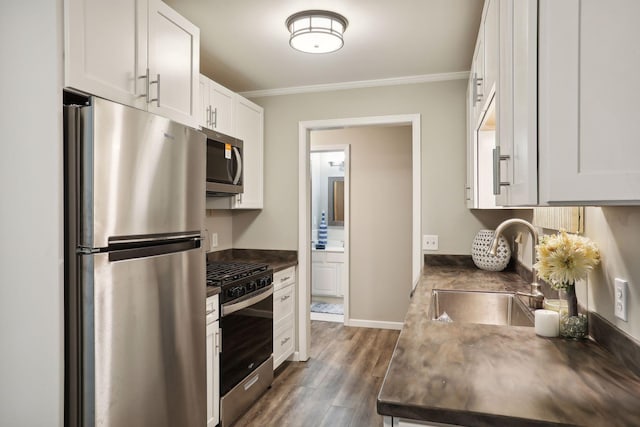 kitchen with dark countertops, stainless steel appliances, crown molding, and a sink